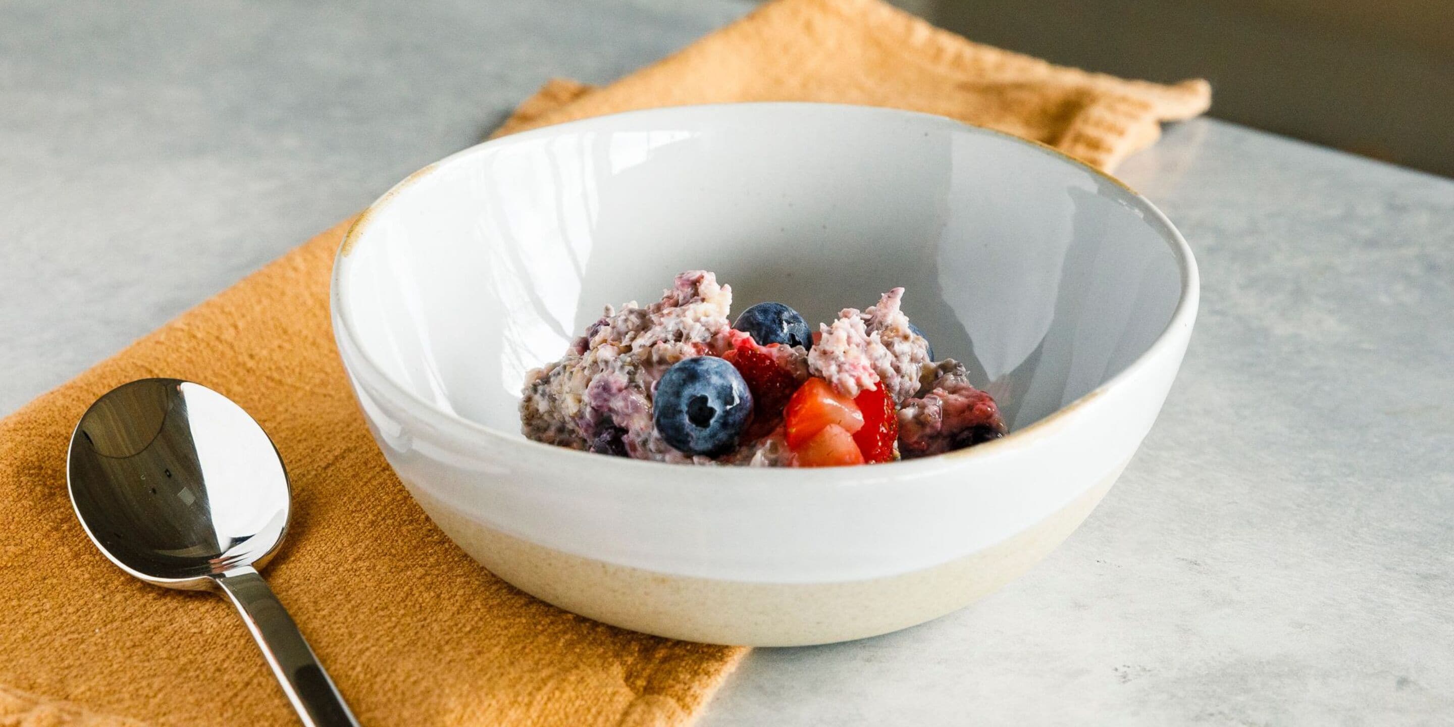 Un tazón de avena con arándanos y fresas sobre un plato blanco, colocado sobre una superficie de mármol con una cuchara a un lado.