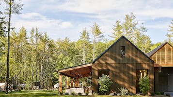 A modern wooden cabin with a covered patio, surrounded by a forest.
