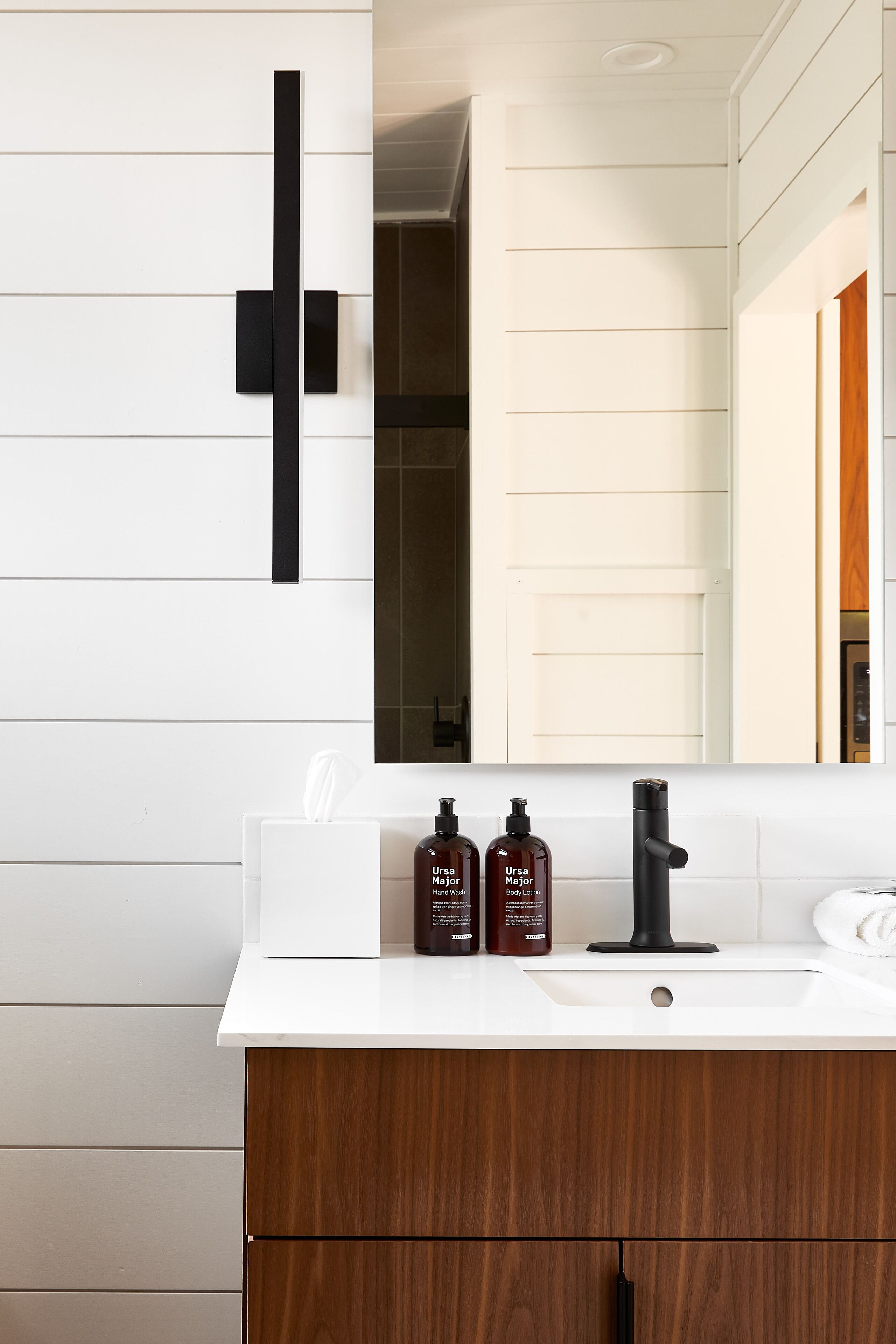 Un baño moderno con tocador blanco, grifo negro y dos botellas de jabón corporal Ursa.