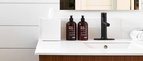 A modern bathroom with a white vanity, a black faucet, and two bottles of Ursa body wash.