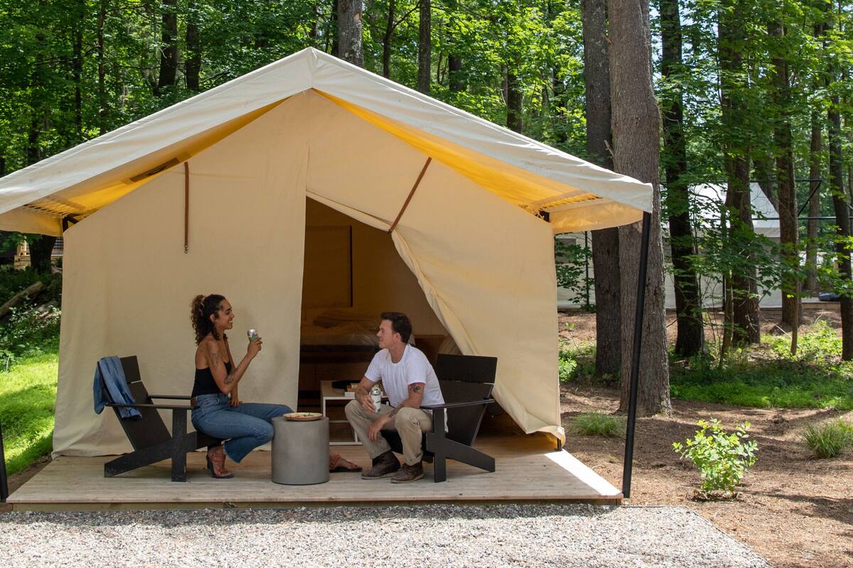 Una carpa con dos sillas y una mesa, rodeada de árboles.