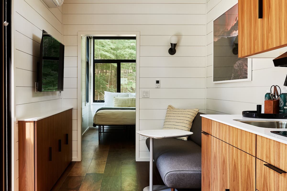 Cocina compacta con armarios de madera, estufa integrada y ventana con vistas a un bosque.