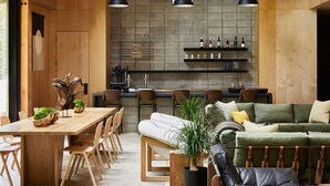 Un interior moderno con una mesa de comedor de madera, sillas, un sofá y una zona de bar con botellas de vino.