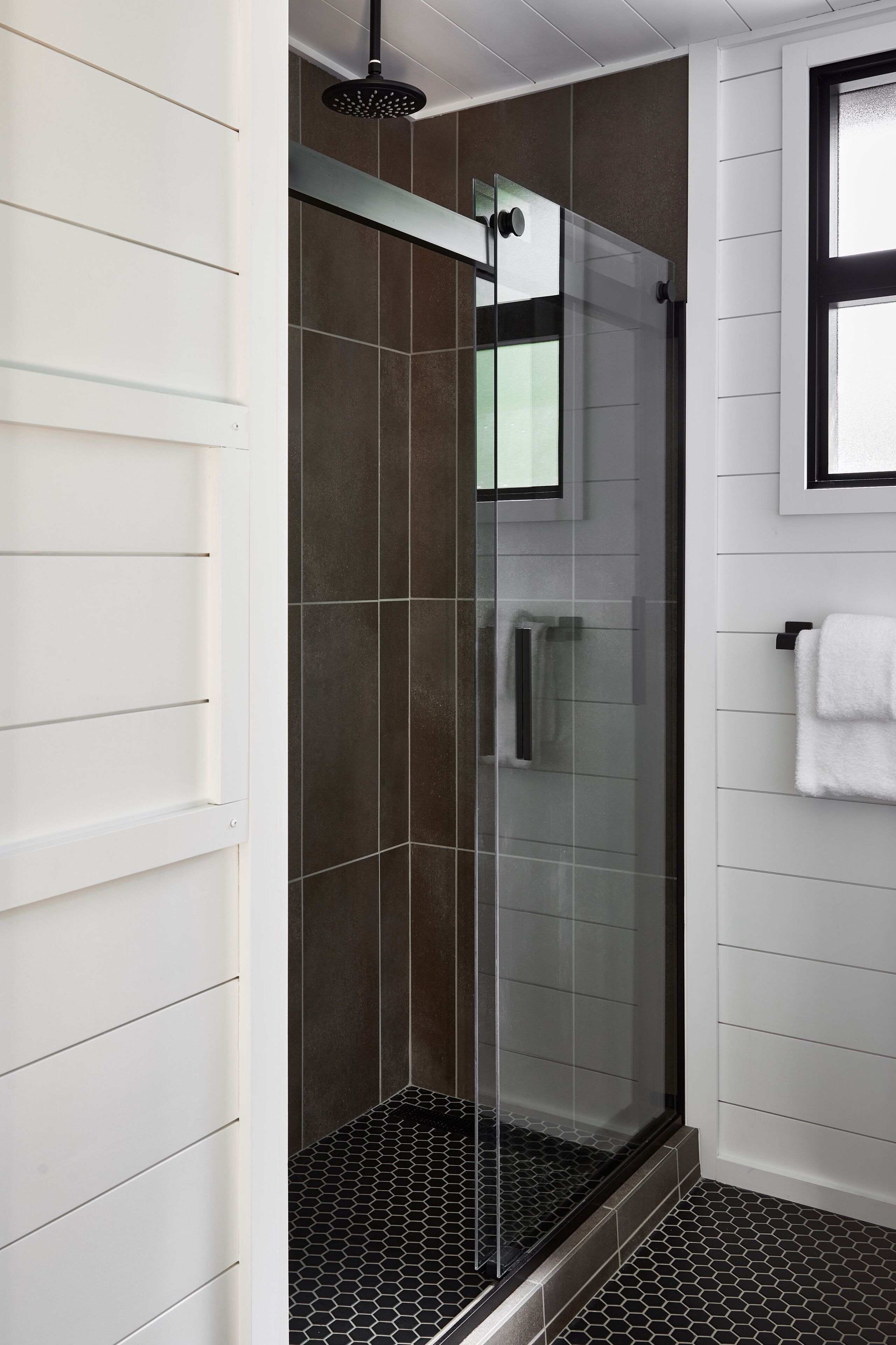 Un baño moderno con ducha de vidrio, paredes blancas y piso de baldosas.
