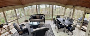 A covered outdoor area with wicker furniture, a glass table, and a view of trees and a house.