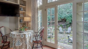 Une pièce chaleureuse avec une table à manger, des chaises, un téléviseur et une vue sur le jardin grâce à de grandes fenêtres.