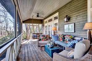 A wooden porch with wicker furniture, a ceiling fan, and a view of trees. - Norman Ridge: In-Town Charming Home w/ Mountain Views, Firepit | Pet Friendly (Highlands)