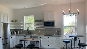 Una cocina moderna con armarios blancos, un refrigerador de acero inoxidable, un microondas y una zona de comedor con taburetes de bar.