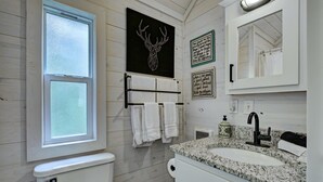 A bathroom with a toilet, a sink with a granite countertop, a mirror, and a window. - Owl's Den: Easy Walk to Main Street | Adorable Tiny Home w/ Screened Porch (Highlands)