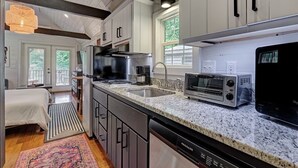 A modern kitchen with white cabinets, a granite countertop, a built-in microwave, and a dishwasher. - Owl's Den: Easy Walk to Main Street | Adorable Tiny Home w/ Screened Porch (Highlands)