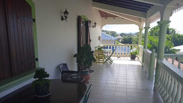 A covered outdoor area with a table and chairs, potted plants, and a view of the surrounding landscape. - 5 Bedroom Villa in Le Lamentin (Le Lamentin)