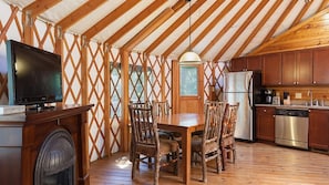 A wooden interior with a dining table, chairs, a television, and a kitchen area.