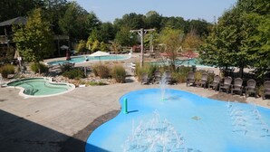 A swimming pool with a fountain feature, surrounded by lounge chairs and a building in the background.