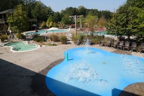 A swimming pool with a fountain feature, surrounded by lounge chairs and a building in the background.