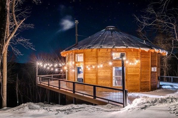 A wooden cabin with a balcony, string lights, and a chimney.