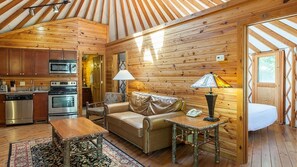 A cozy cabin interior with wooden walls, a kitchenette, a sofa, a table, and a lamp.