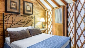 A wooden bedroom with a bed, a nightstand, and a window with curtains.