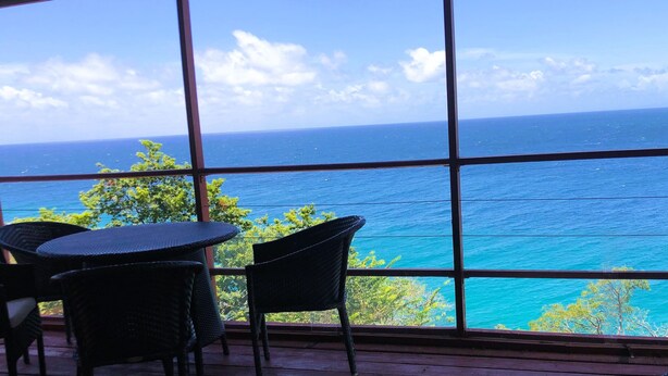 A room with large windows offering a view of the ocean. There are wicker chairs and a small table. - Top Seaview Apartment with pool (Scarborough)