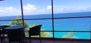 A room with large windows offering a view of the ocean. There are wicker chairs and a small table. - Top-floor apartment with a view of the ocean and the pool (Scarborough)