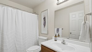Une salle de bain avec un rideau de douche, des toilettes, un lavabo et un miroir.