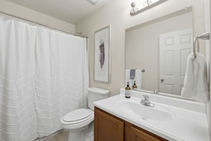 A bathroom with a shower curtain, toilet, sink, and mirror. - The Las  Alturas  House (Alamogordo)