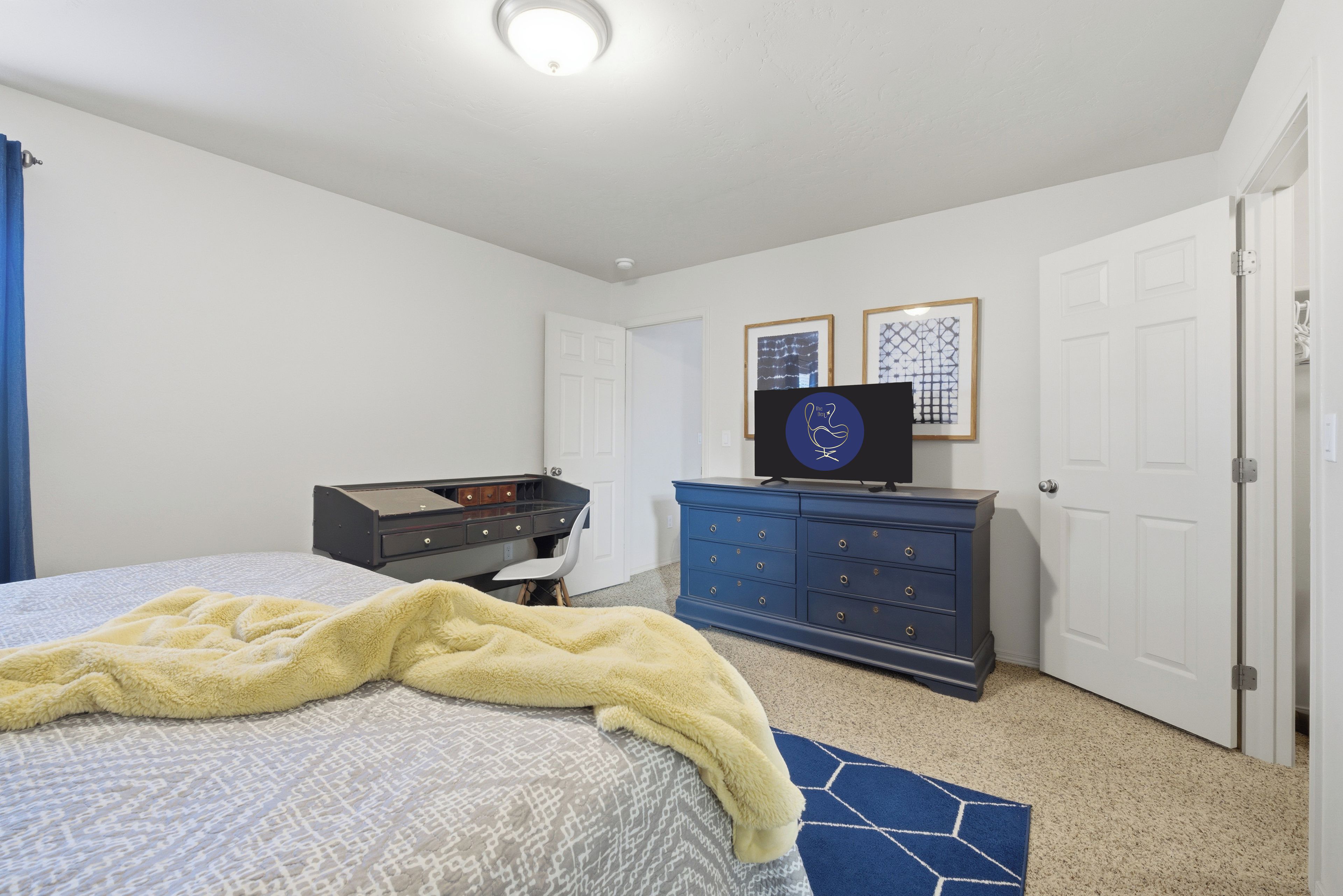 A bedroom with a bed, a dresser, a desk, and a television.