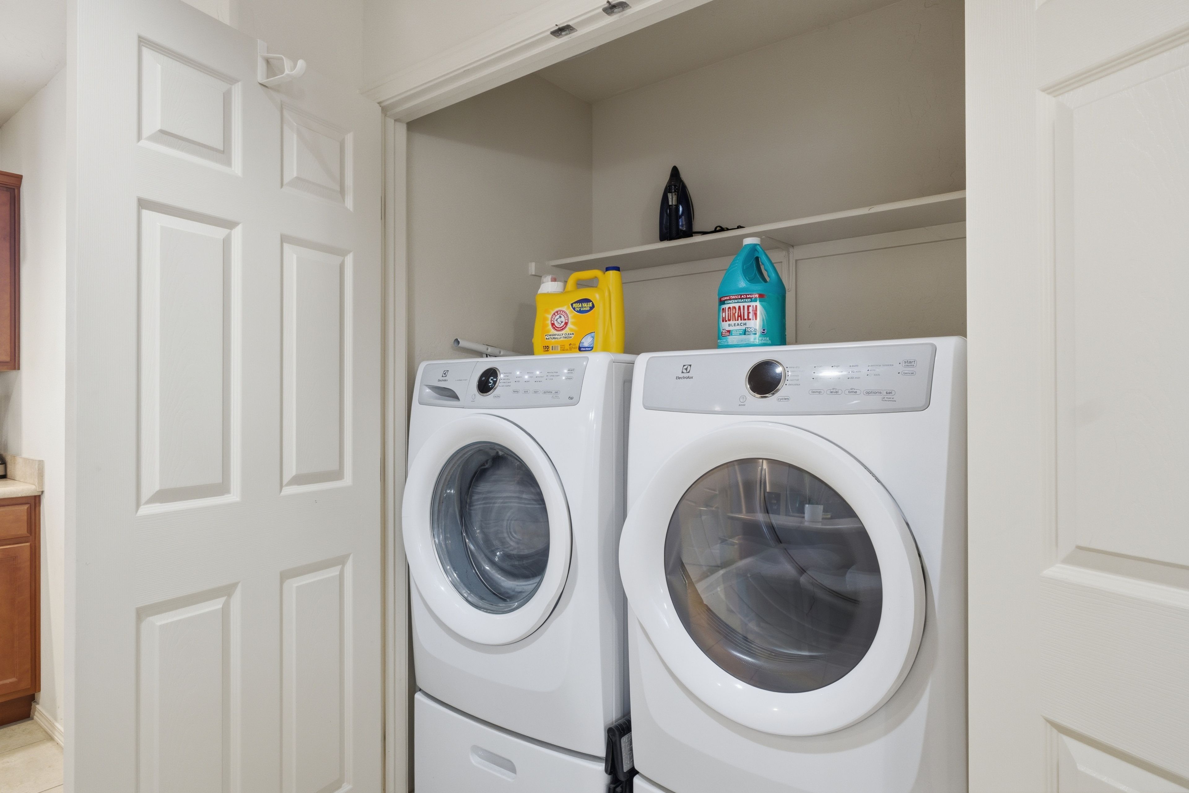 A laundry room with two front-loading washing machines and shelves above them holding cleaning supplies.