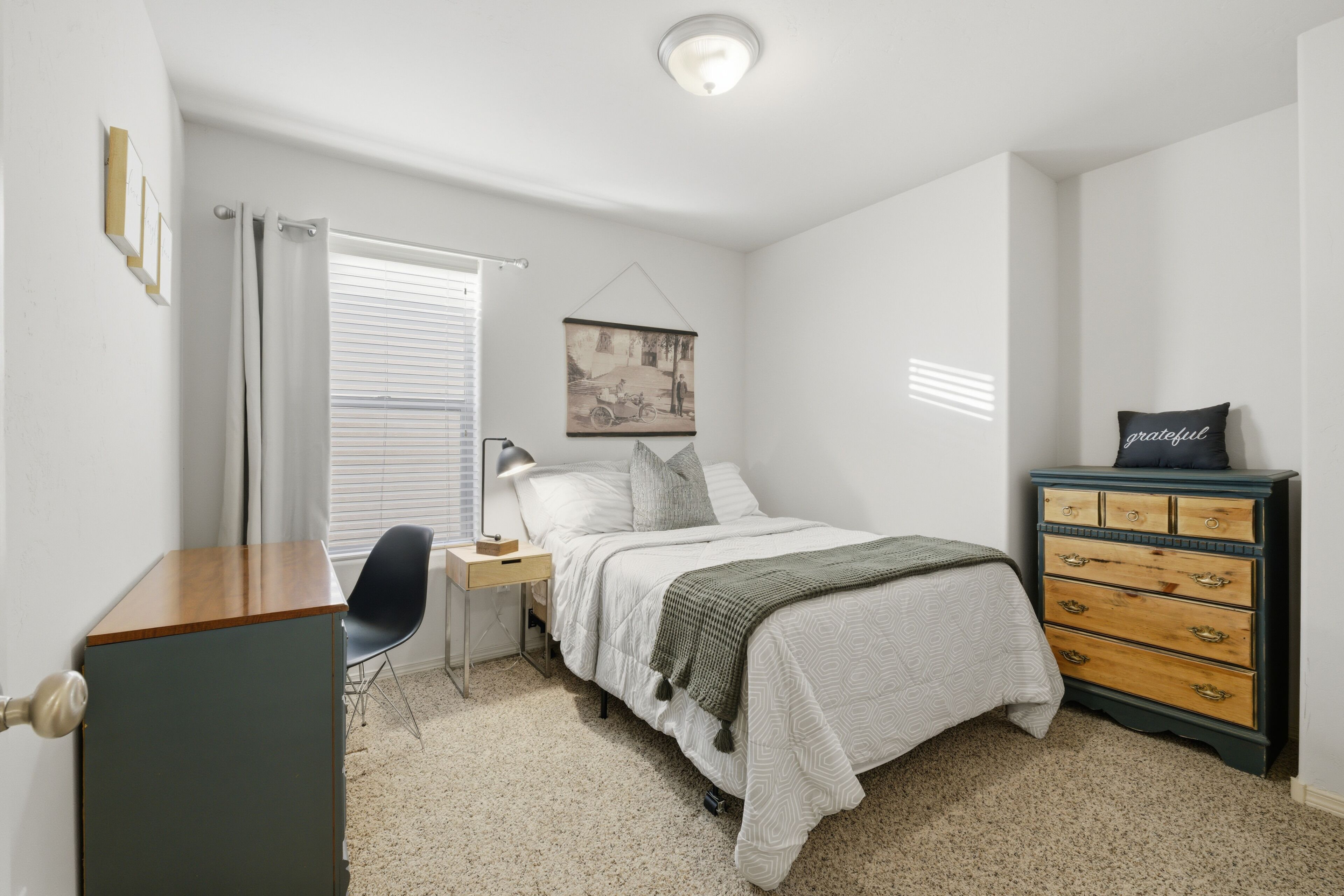 Een slaapkamer met een bed, een dressoir, een stoel, een nachtkastje, een lamp en een aan de muur hangend schilderij.