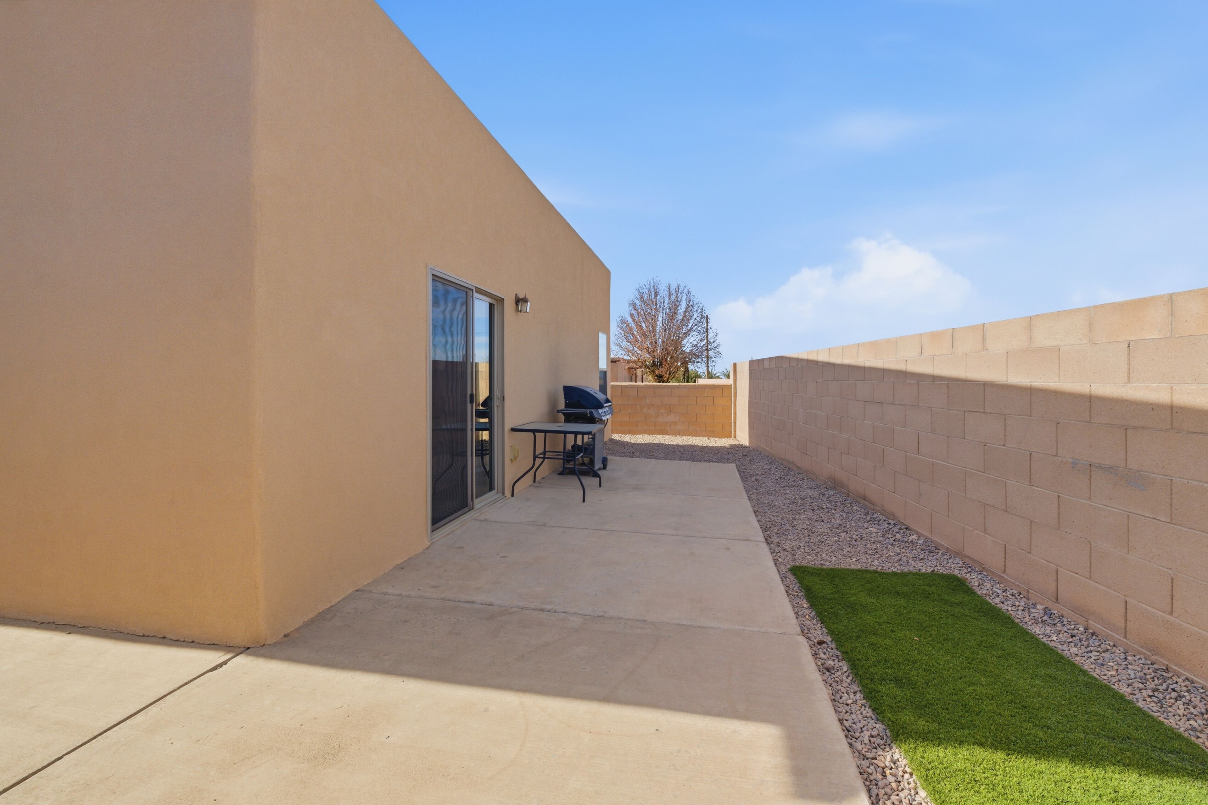 A patio area with a concrete floor, a small table, and a grill.