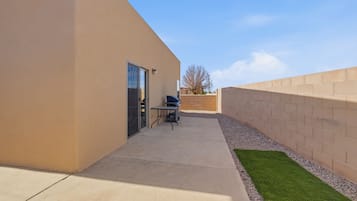 A patio area with a concrete floor, a small table, and a grill.