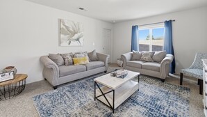 Un salon avec deux canapés, une table basse, un tapis et un tableau accroché au mur.