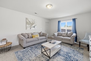 A living room with two sofas, a coffee table, a rug, and a painting on the wall. - The Las  Alturas  House (Alamogordo)