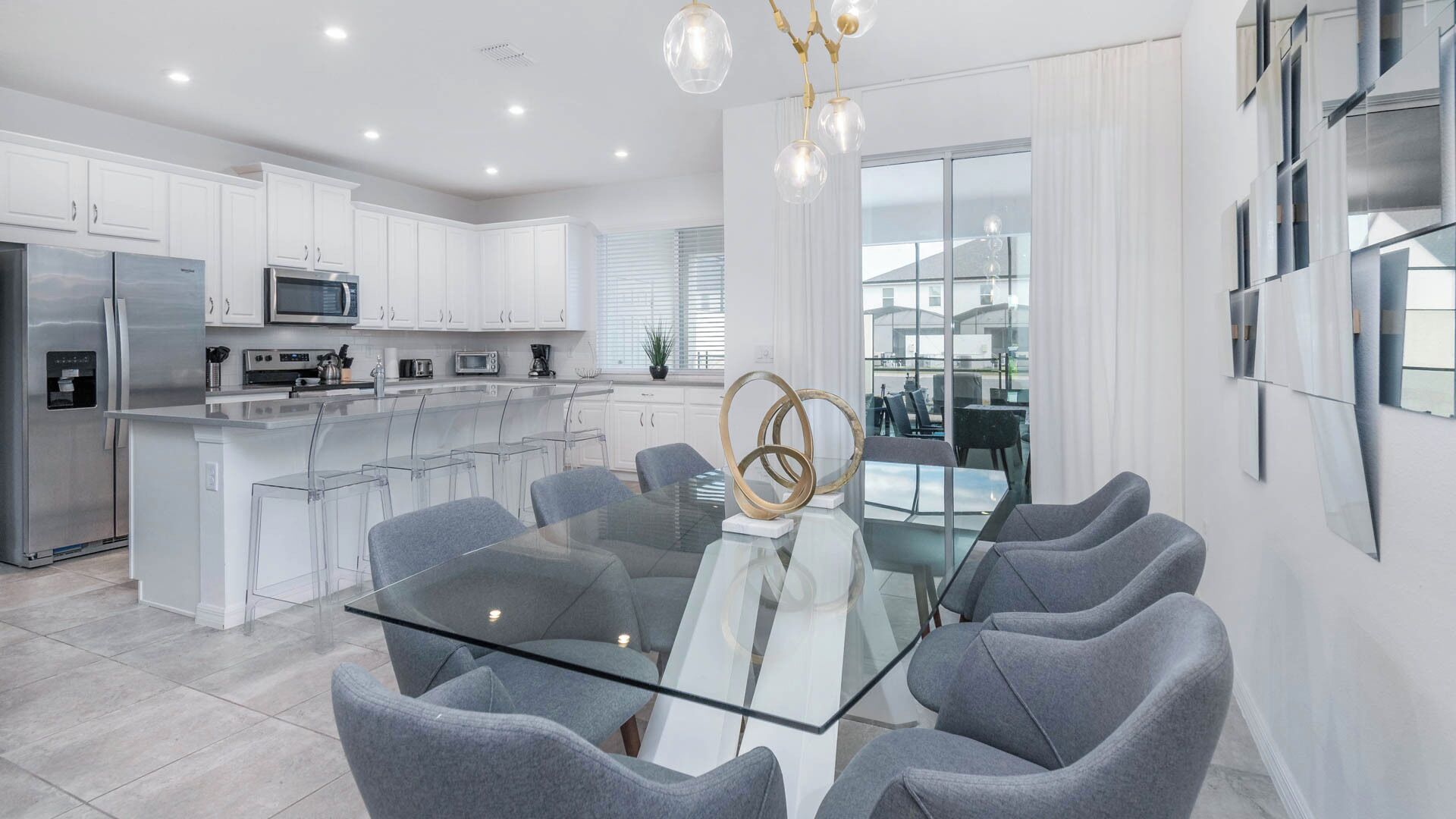 A modern kitchen with white cabinets, stainless steel appliances, and a glass dining table with grey chairs.