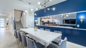 A modern kitchen with a large island, a dining area with a white table and grey chairs, and a blue accent wall. - New Listing! Champions Gate Resort, 10mi to Disney & 21mi to Universal - GRH488628 (Davenport)