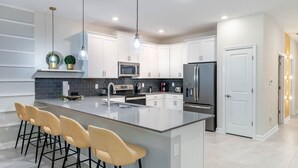 A modern kitchen with white cabinets, a large island with bar stools, a stainless steel refrigerator, and a microwave. - New Listing! Champions Gate Resort, 10mi to Disney & 21mi to Universal - GRH488628 (Davenport)