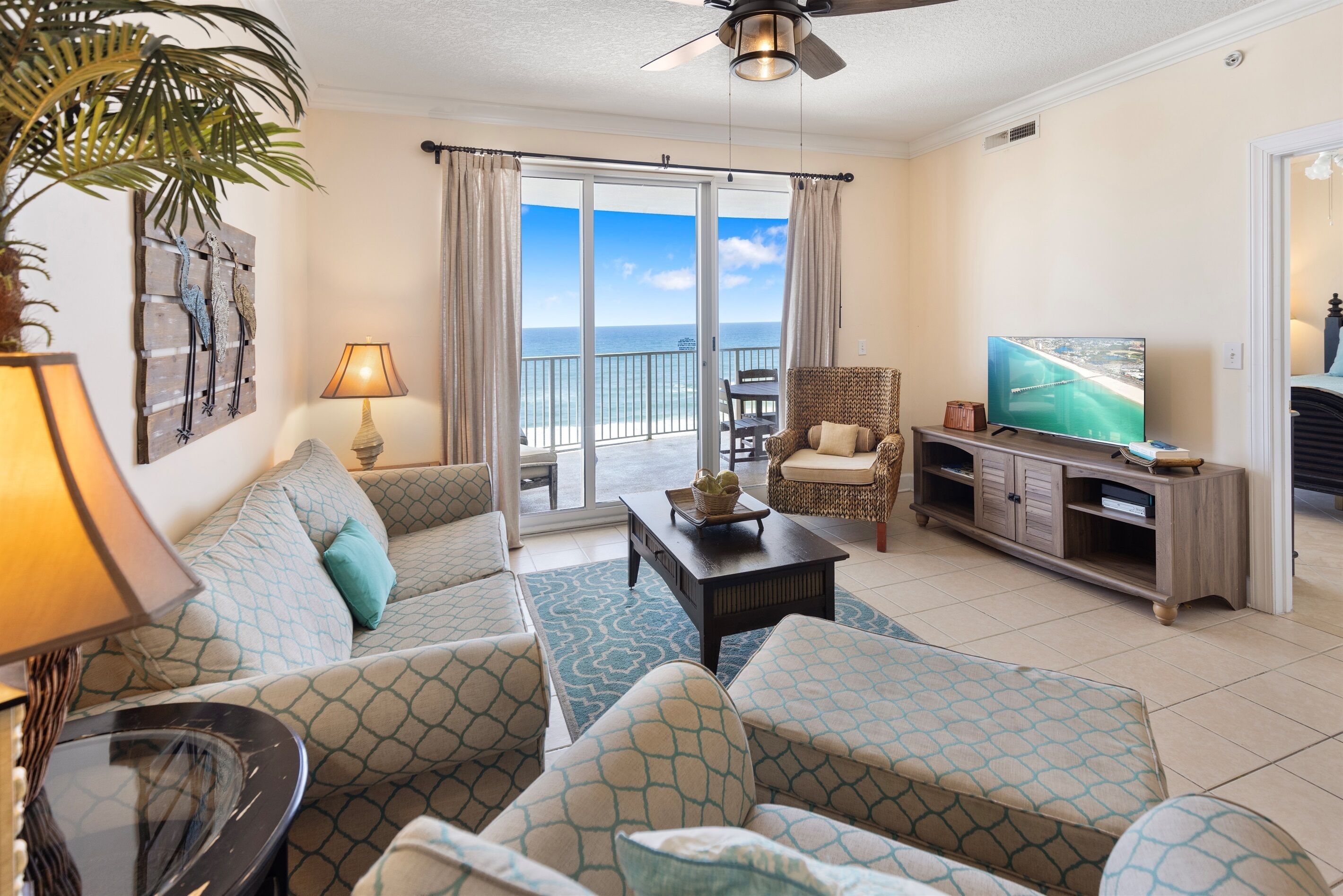 A living room with a sofa, chairs, a coffee table, a TV, and a view of the ocean through large sliding doors.