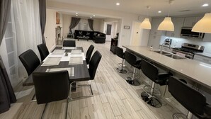 Une cuisine moderne équipée d’appareils électroménagers en acier inoxydable, un coin repas avec une longue table et des chaises, et un salon avec un canapé et une table basse.