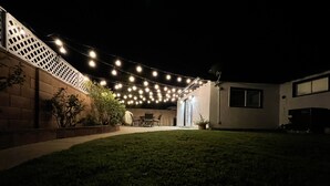 Un jardin avec une terrasse, des guirlandes lumineuses et une pelouse.