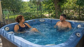 Ein Whirlpool mit zwei Personen, umgeben von einer Ziegelmauer und Pflanzen.