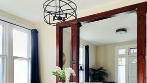 Comedor con mesa y sillas de madera, lámpara colgante y vista a otra habitación con sofá y planta.