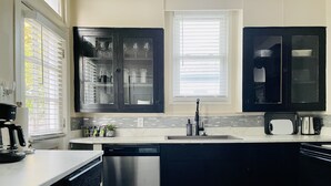 Una cocina moderna con armarios oscuros, un lavavajillas de acero inoxidable y una ventana con persianas.
