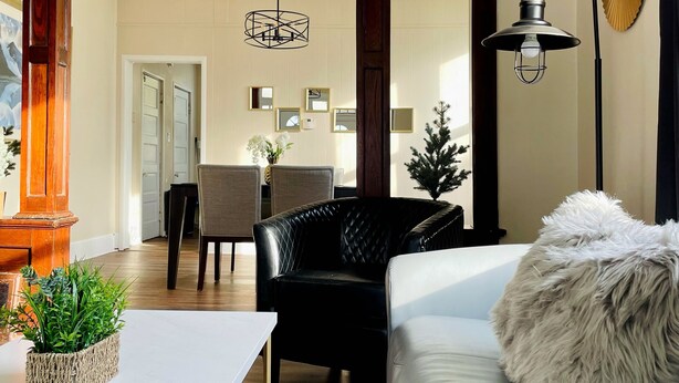 Una sala moderna con un sofá blanco, un sillón de cuero negro, una mesa de centro de madera y una zona de comedor al fondo.