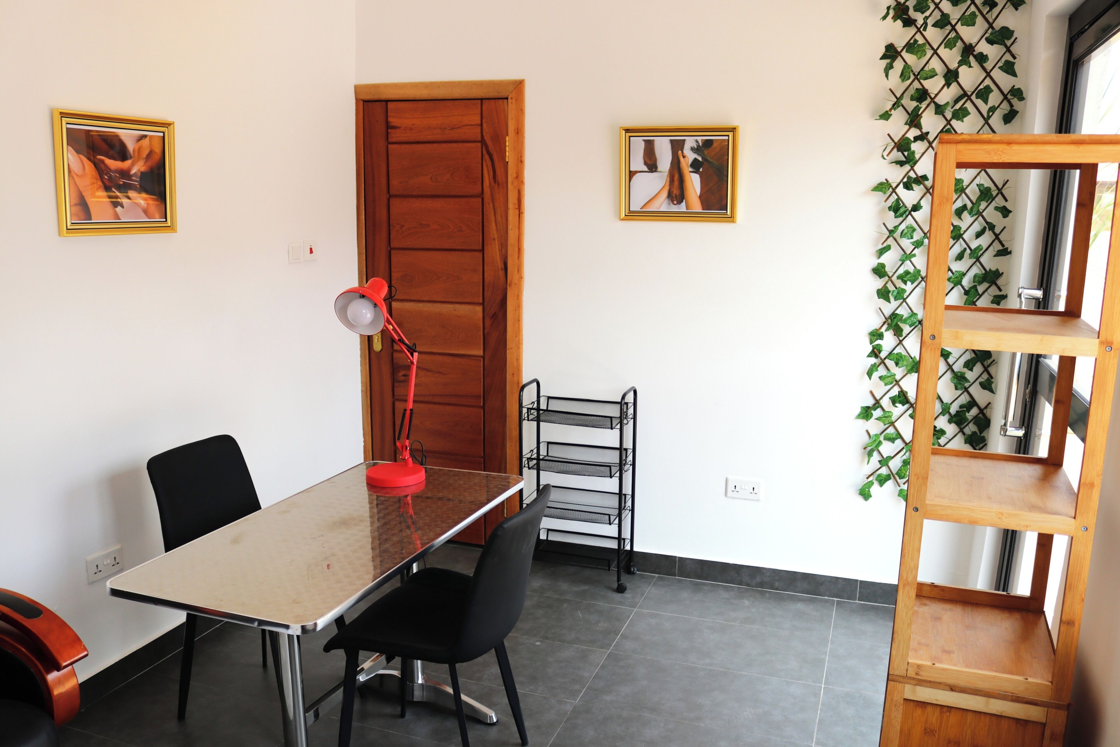 A dining area with a table, chairs, a red lamp, a wooden door, and a wall-mounted rack.