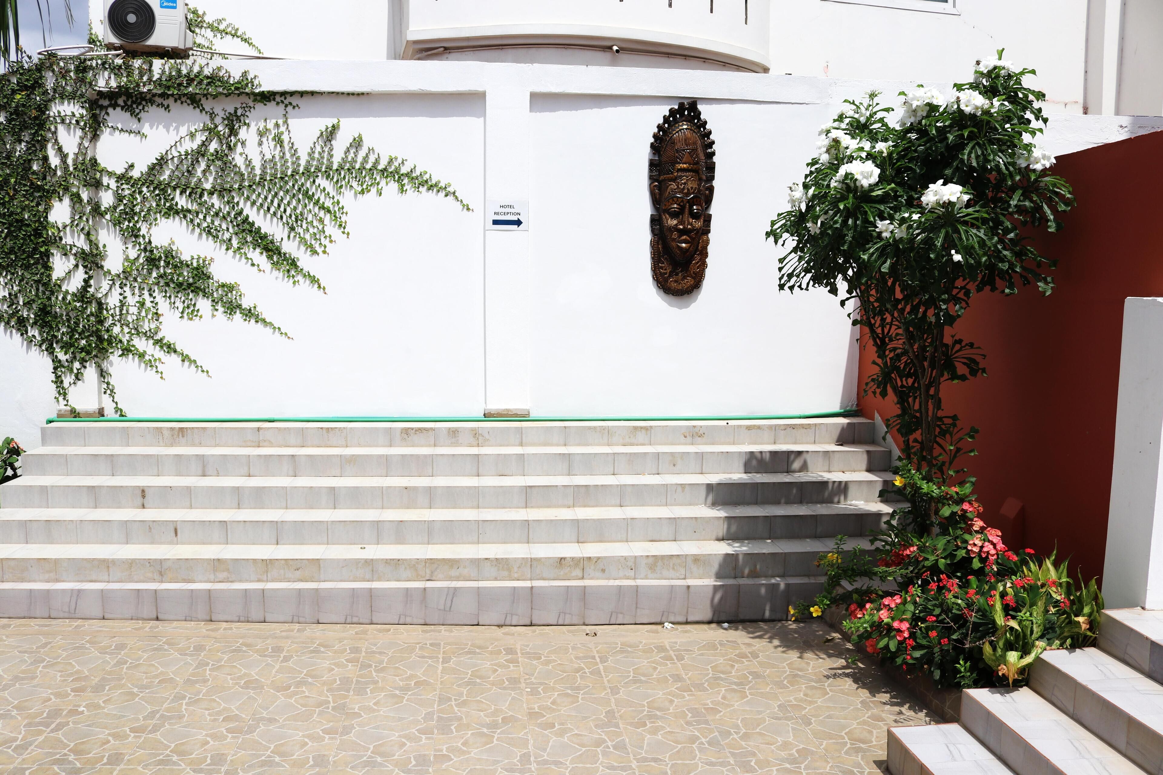 L’entrée d’un hôtel, avec une façade blanche, une enseigne indiquant la réception, un élément décoratif en bois et des marches menant à l’entrée.