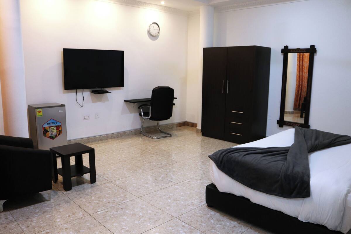 Una habitación de hotel con cama, escritorio, silla, televisor y armario.