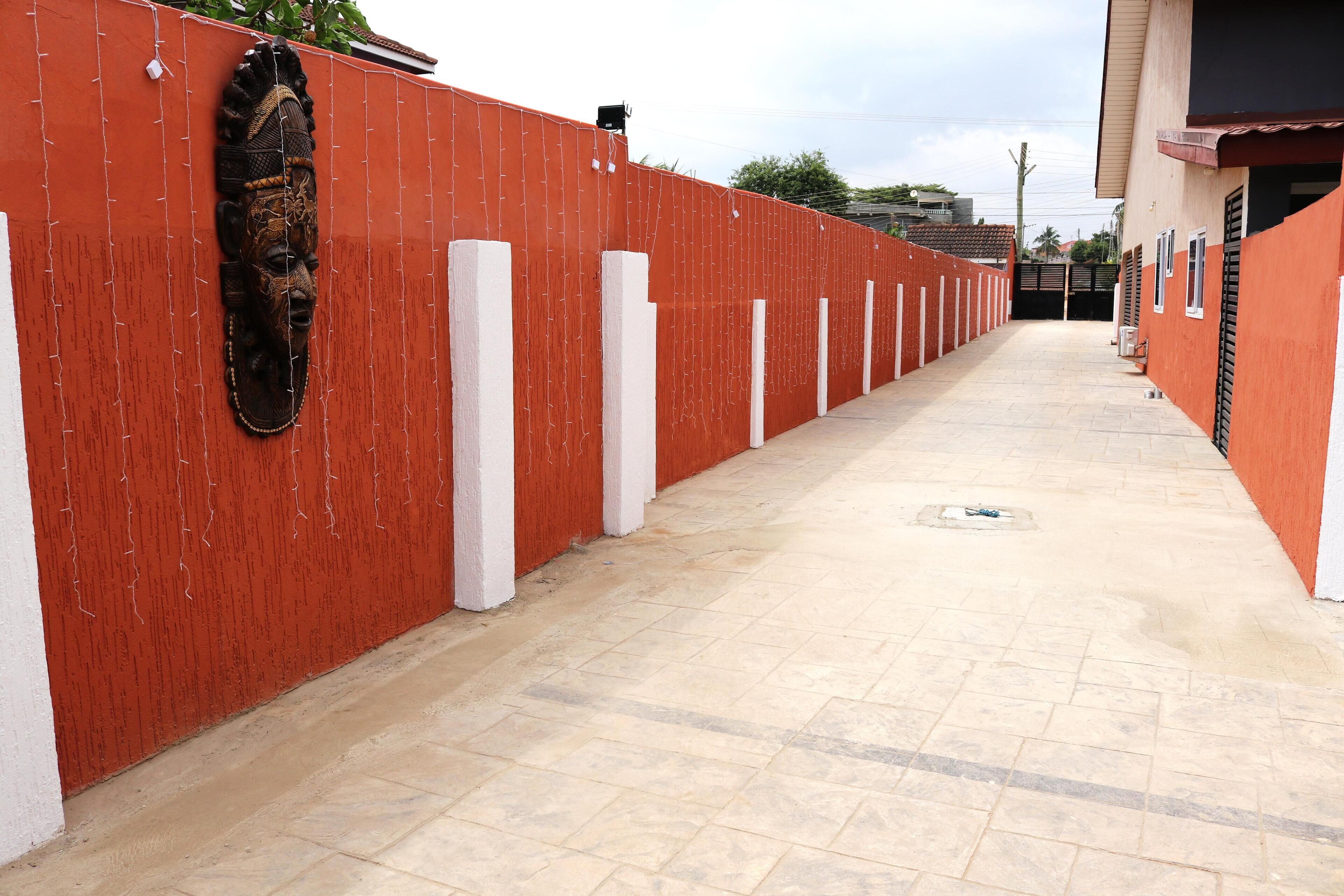 Un couloir avec un mur rouge, des piliers blancs et un sol carrelé.