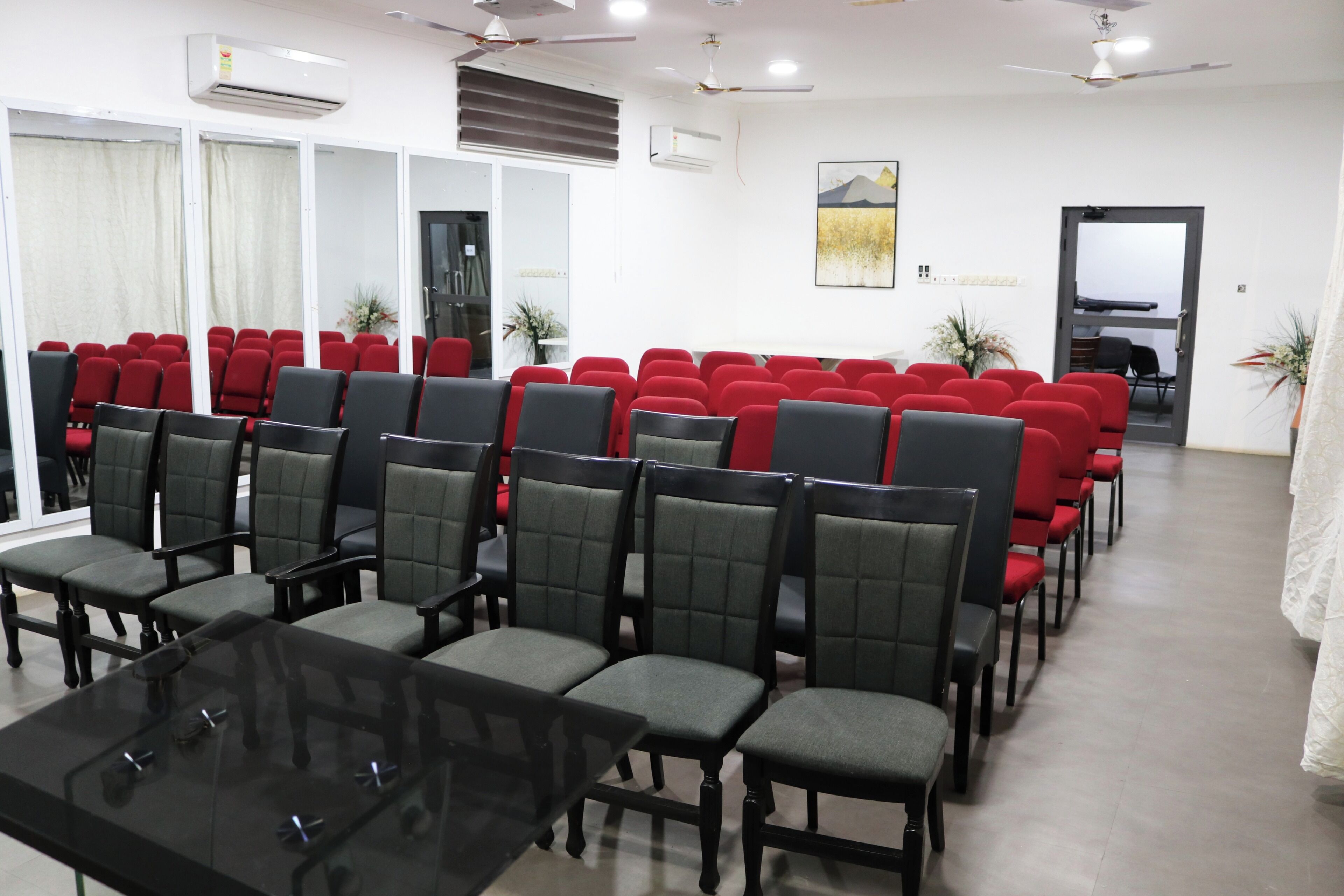 A conference room with rows of red and black chairs, a glass table, and ceiling fans.