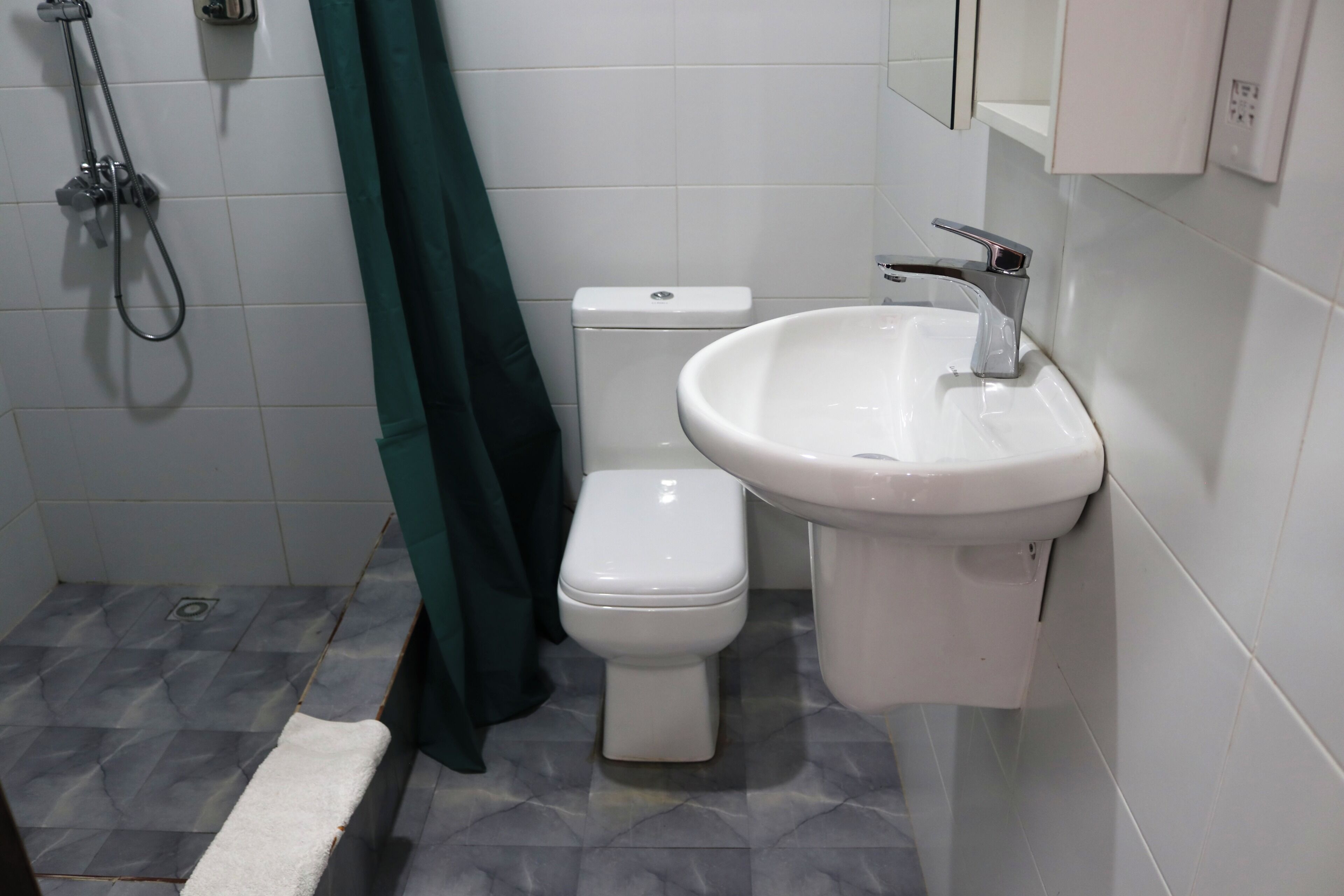 A bathroom with a toilet, sink, shower, and green curtain.