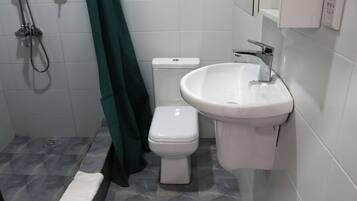 A bathroom with a toilet, sink, shower, and green curtain.