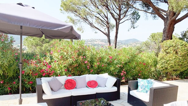 An outdoor seating area with wicker furniture, a white sofa with watermelon-themed cushions, and a large umbrella. - 100m2 house with private pool (Sainte-Maxime)